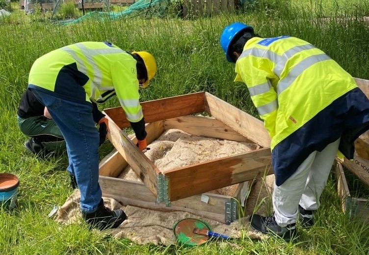 People in high vis and hard hats building raised wooden beds in grassy area